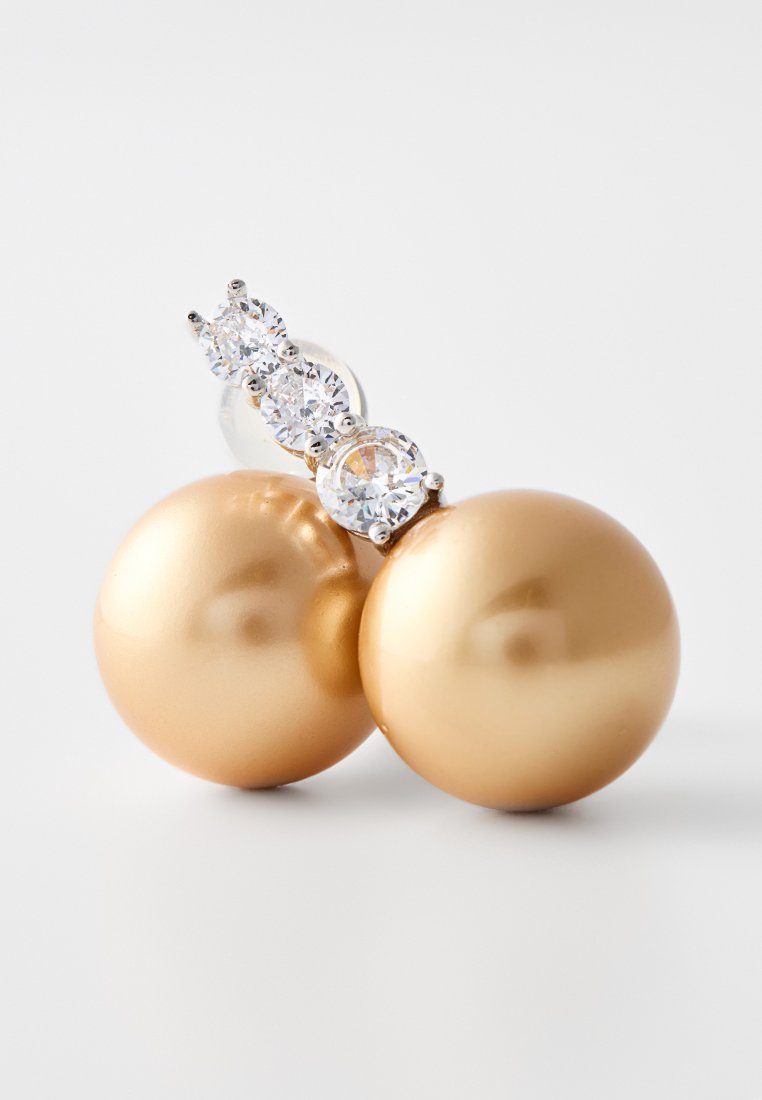 Pendientes esféricos de oro con un acabado suave y brillante, que presentan una fila de tres piedras preciosas redondas y transparentes en un soporte de plata.