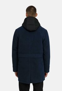 Námornícky kabát s čiernou vypchanou kapucňou, so strihom do priamej línie, dlhými rukávmi a minimalistickým dizajnom. Hladká textura, žiadne viditeľné vzory.