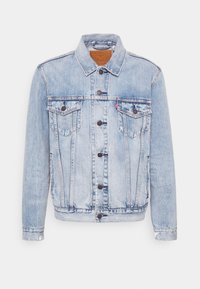 Ljusblå denimjacka med två bröstfickor, knappstängning och klassisk krage. Har slitna områden och kontrasterande sömnad.