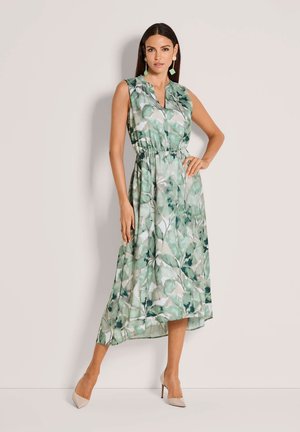 Ärmelloses Kleid mit Blumenmuster in Grün- und Weißtönen. Es hat einen V-Ausschnitt, einen elastischen Taillenbund und einen fließenden Saum. Kombiniert mit Nude-Pumps.