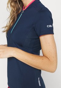 Top deportivo azul marino con mangas cortas, cuello con cremallera, paneles de malla y detalles en rosa. Fabricado con material transpirable para un rendimiento activo.