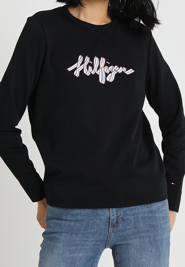 Czarna bluza z okrągłym dekoltem, z jasnym logo na przodzie i ściągaczami na mankietach. Noszona z niebieskimi dżinsami.