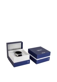 Zwarte horloge met zilveren accenten in een twee-kleurige blauwe en witte doos. Het horloge heeft een strak gezicht en een gestructureerde zwarte band.