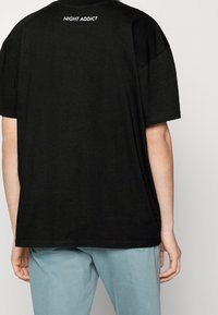 Černé oversized tričko z bavlny, s krátkými rukávy a logem "NIGHT ADDICT" v bílé barvě na horní části zad. Volný střih.