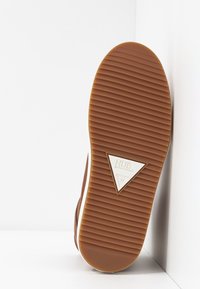 Brown rubber shoe sole with horizontal grooves, a white triangular logo, and size 37 indicated. The edge is smooth with a rounded shape.