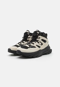 Leichte Wanderschuhe mit einem oberen Teil aus beigem Stoff, schwarzen Akzenten, einer dicken schwarzen Gummisohle und einer Schnürung für einen sicheren Sitz.
