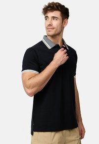 Tricou polo negru cu un guler gri contrastant, având accente albe pe guler și pe mâneci. Fabricat dintr-un material neted, texturat.