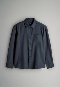 Granatowa koszula z długim rękawem, uszyta z gładkiego materiału, z klasycznym kołnierzykiem, zapięciem na guziki z przodu oraz jedną kieszonką na piersi.