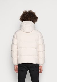 Een puffy lichtroze jas met capuchon, voorzien van een gewatteerd ontwerp, elastische manchetten en een rechte zoom. Draag het over zwarte broek.
