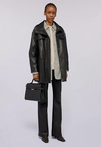 Schwarze Lederjacke in Übergröße, weiß-schwarz gestreiftes Hemd, schwarze Schlaghosen und eine kleine schwarze Handtasche mit Verschluss aus Metall.