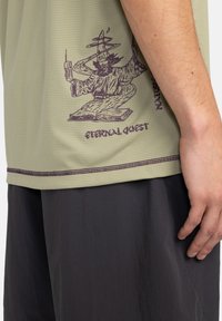 Short-sleeve, light green t-shirt with a textured finish, featuring a purple wizard graphic and "Eternal Quest" text near the hem.