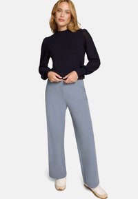 Pull bleu marine avec des manches bouffantes texturées, associé à un pantalon large bleu clair et des baskets blanches, offrant une coupe décontractée et des lignes épurées.