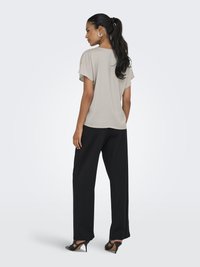 Atasan pendek warna beige cerah, model longgar, dipadukan dengan celana lebar hitam, dan sepatu hak tinggi hitam. Teksurnya halus, desainnya sederhana.