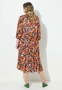 Vestido de estampado de leopardo en naranja, con un dobladillo acampanado en capas, mangas tres cuartos y un corte holgado. Combinado con tacones de bloque verdes.