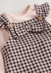 Top rosa con salopette a motivo houndstooth nero. Presenta un collo volantino e bottoni in legno con dettaglio a fiocco. Tessuto testurizzato.