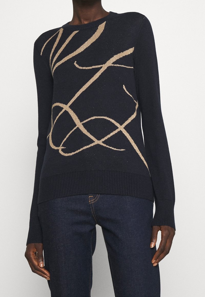 Marinblå tröja med en mjuk textur som har en beige abstrakt design. Ribbade sömmar vid nederkant och ärmar, rundad halslinning och en slank silhuett.