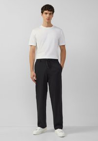 Zwarte broek met een relaxte pasvorm, koord in de taille, gecombineerd met een effen wit shirt met korte mouwen en witte sneakers. Minimalistisch design.