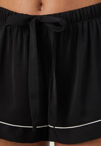 Svarta shorts med resår i midjan, med en framknutning och vit piping runt fållen. Lätt material med en slät yta.