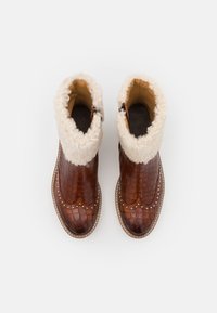 Botas de cuero marrón con estampado de cocodrilo, con un puño de borrego blanco y pequeños Studs metálicos a lo largo de la suela. Cierre con cremallera en el costado.