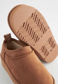 Barna nubuk slip-on cipők, texturált gumitalppal, puha béléssel és szőtt hurkkal a sarkában a könnyű felhúzás érdekében.