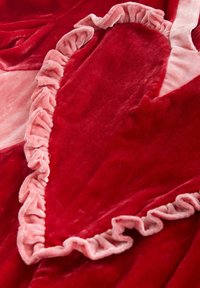 Roter Samtstoff mit einer großen Herzform, umrandet von weichem, rosa Rüschensaum, der ein strukturiertes und plüschiges Design schafft.