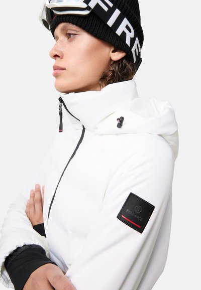 Biała ocieplana kurtka z wysokim kołnierzem, czarnymi akcentami i zamkiem. Posiada naszywkę z logo na rękawie oraz smukły design.