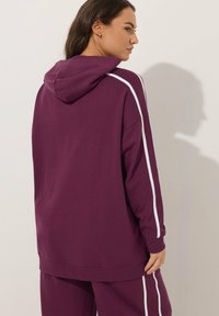 Körsbärsröd huvtröja med vita sidojackor, med en avslappnad passform och ribbade ärmslut. Mjuk textur, slätt tyg och minimalistisk design.