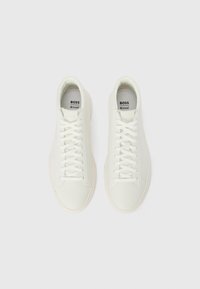Zapatillas de deporte de cuero blanco con superficie suave, diseño con cordones y puntera redonda. Presentan un estilo minimalista y un logotipo sutil en la lengüeta.