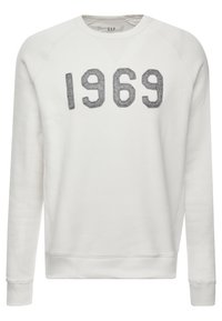 Sweatshirt blanc à manches longues et col rond avec le texte texturé « 1969 » en gris sur la poitrine, des poignets et un ourlet côtelés.