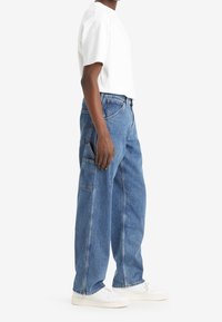 Witte t-shirt met korte mouwen, gecombineerd met losse blauwe denim jeans. De jeans hebben een zijzak en een recht gesneden ontwerp.