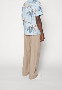 Camicetta a maniche corte, con motivo floreale blu, realizzata in tessuto leggero, abbinata a pantaloni beige larghi e scarpe da ginnastica bianche.