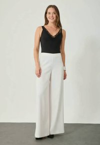 Czarny bodysuit z koronkowymi wykończeniami w połączeniu z białymi spodniami o wysokim stanie i szerokich nogawkach, wykonanymi z gładkiego materiału o minimalistycznym designie.