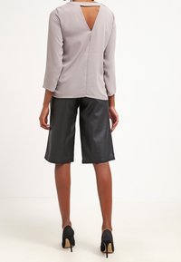 Lichtgrijze blouse met lange mouwen en een uitsnede op de rug, gecombineerd met hoge zwarte leren shorts en zwarte hoge hakken. Soepele textuur.