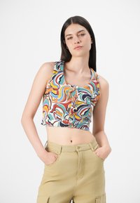 Débardeur court multicolore avec un motif tourbillonnant, encolure ronde et boutons sur le devant. Porté avec un pantalon cargo beige.