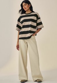 T-shirt rayé en beige et vert foncé, à manches courtes, coupe décontractée. Associé à un pantalon beige à jambe large, doté de poches avant et de coutures discrètes.