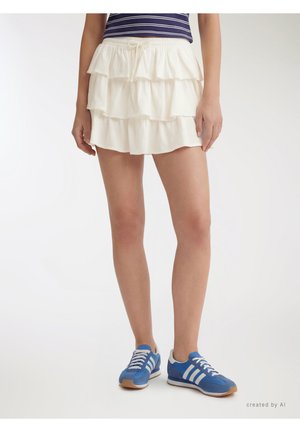 Donna che indossa una minigonna bianca a strati, una maglietta a righe blu e bianche e sneakers blu con righe bianche, in piedi su sfondo bianco.