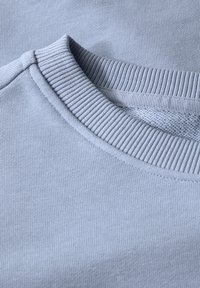 Sweatshirt bleu clair avec un col côtelé et une texture lisse, présentant un design simple et un tissu doux adapté à une tenue décontractée.