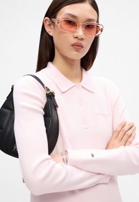 Svetloružová polokošeľa s dlhým rukávom, golierom a zapínaním na gombíky, skombinovaná s čiernou koženou kabelkou na rameno s zlatým kováním.