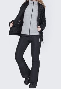 Czarne ocieplane spodnie i szara polarowa kurtka z wysokim kołnierzem, z zamkami błyskawicznymi i dopasowanym krojem, noszone z czarnym obuwiem.