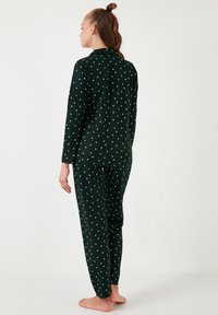 Ensemble de pyjama vert foncé avec motif d'étoiles blanches. Haut à manches longues avec col et pantalon assorti à taille élastique. Tissu doux et confortable.