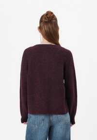 Maroon knitted sweater with a relaxed fit, long sleeves, and a slightly cropped back. Soft texture and ribbed detailing at the hem.