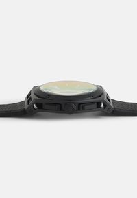 Schwarze Uhr mit einem strukturierten schwarzen Lederarmband, eckigem Metallgehäuse, gewölbtem Glasspiegel mit mehrfarbigem Verlauf und zwei seitlichen Tasten.