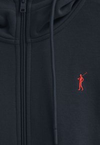 Felpa zip in marinara realizzata in tessuto testurizzato, con logo ricamato di un golfista rosso sul lato sinistro del petto e cappuccio con coulisse.