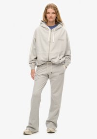 Gray zip-up hoodie with drawstrings, large front pocket, and matching gray sweatpants. Features "Superdry" logo in a subtle tone.
