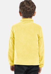 Gele fleece pullover met een hoge kraag, zachte textuur en lange mouwen, achterstevoren gedragen, zonder zichtbare hardware of patronen.