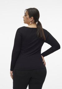 Top negro de manga larga con canalé, escote redondeado, forma ajustada y textura suave, combinado con pantalones negros.