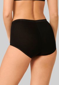 Slip in cotone nero a vita alta con una texture liscia, bordi scallopati sottili e design a copertura totale, mostrato da dietro.