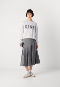 Svetlosivý mikina s logom "GANT", vysoko nastaviteľná sivá plisovaná sukňa a metalické strieborné tenisky s bielymi ponožkami.