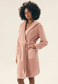 Różowy, pluszowy szlafrok z kapturem, wiązanym paskiem i dwiema przednimi kieszeniami. Zaprojektowany z miękkiego materiału i o długości do kolan.