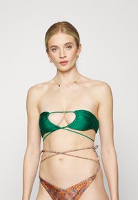 Top de biquíni verde em satin com um corte no centro, apresentando atilhos cruzados. A parte de baixo tem um padrão paisley multicolorido.